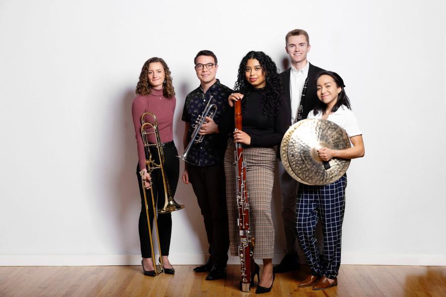 Five students stand together holding brass, woodwind and percussion instruments.