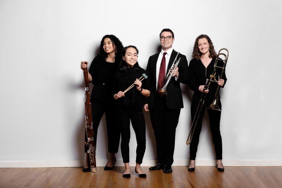 Four students wearing black hold wind and brass instruments.