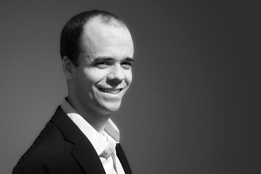 A black and white photo of a man smiling and wearing a white shirt and a black suit jacket.