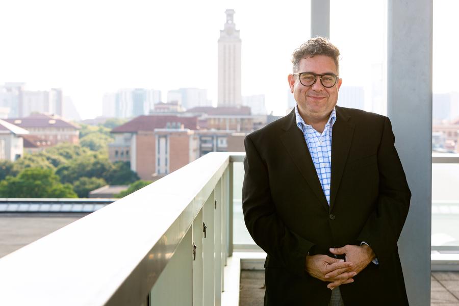 Dean Rivera-Servera stands on a Balcony overlooking the university campus.  The UT tower rises in the background.