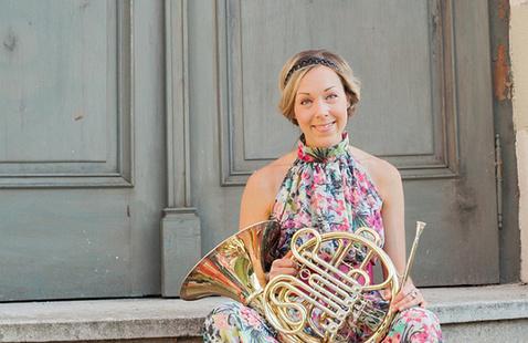 A woman wearing a floral dress sits on steps with a horn in her lap.