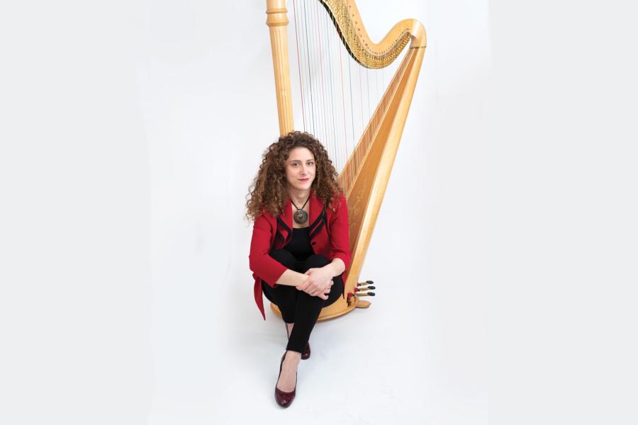 A woman in a red jacket sits at the foot of a harp.