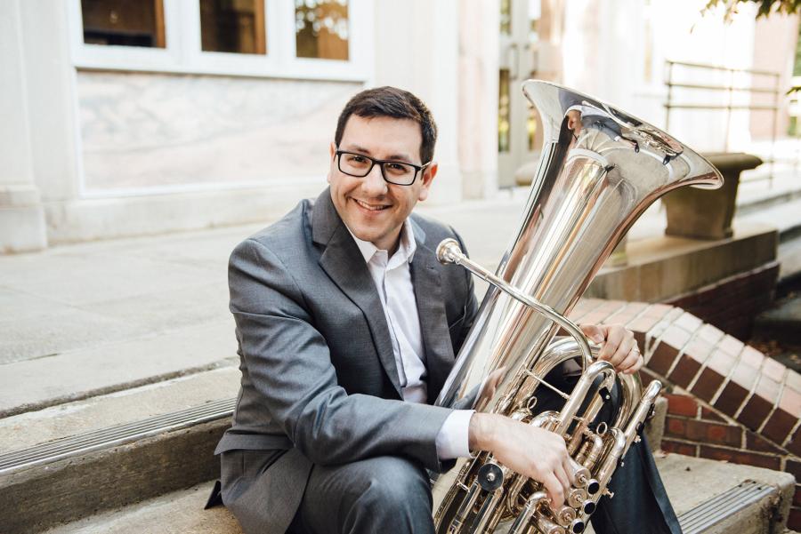 Benavidez sits on stairs outside a building with his tuba on his lap.