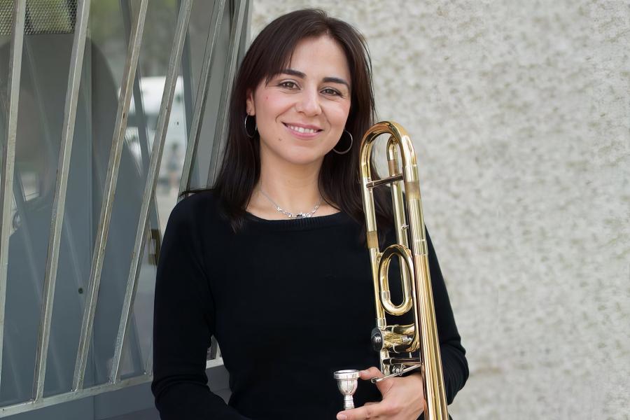 Marcia Medrano stands outside in front of a window holding her trombone.