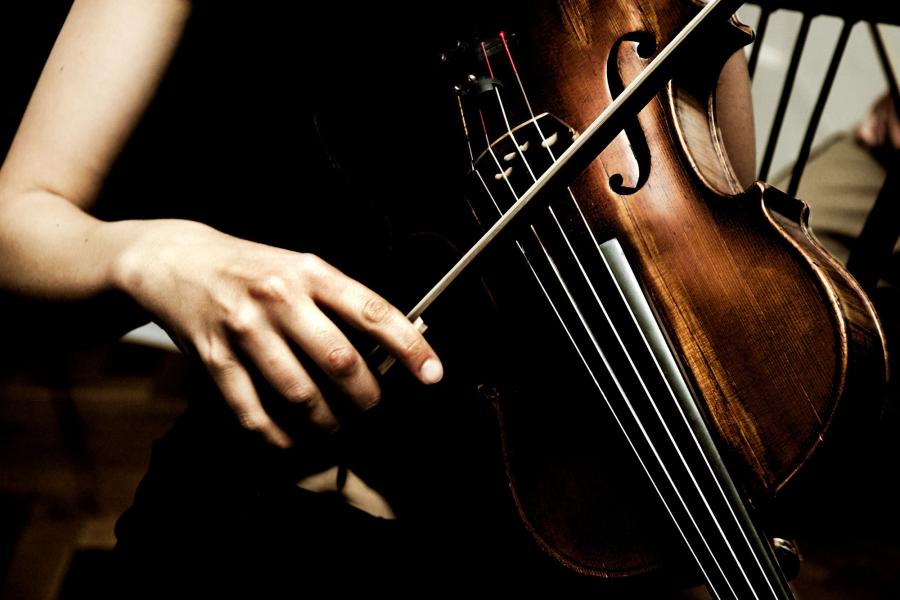 A woman's arm pulls a bow across a dark cello.