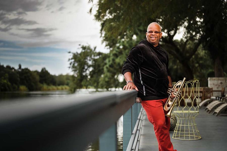 Terence Blanchard leaning on a bridge outside holding his trumpet.