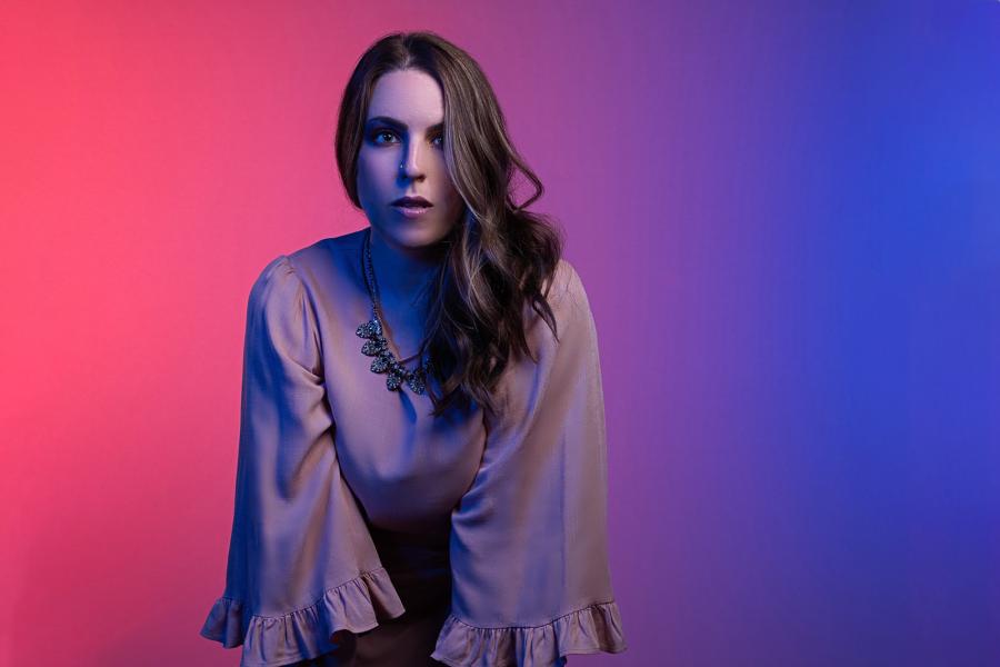 Mezzo soprano Page Stephens in a pink dress in front of a neon pink and blue background.