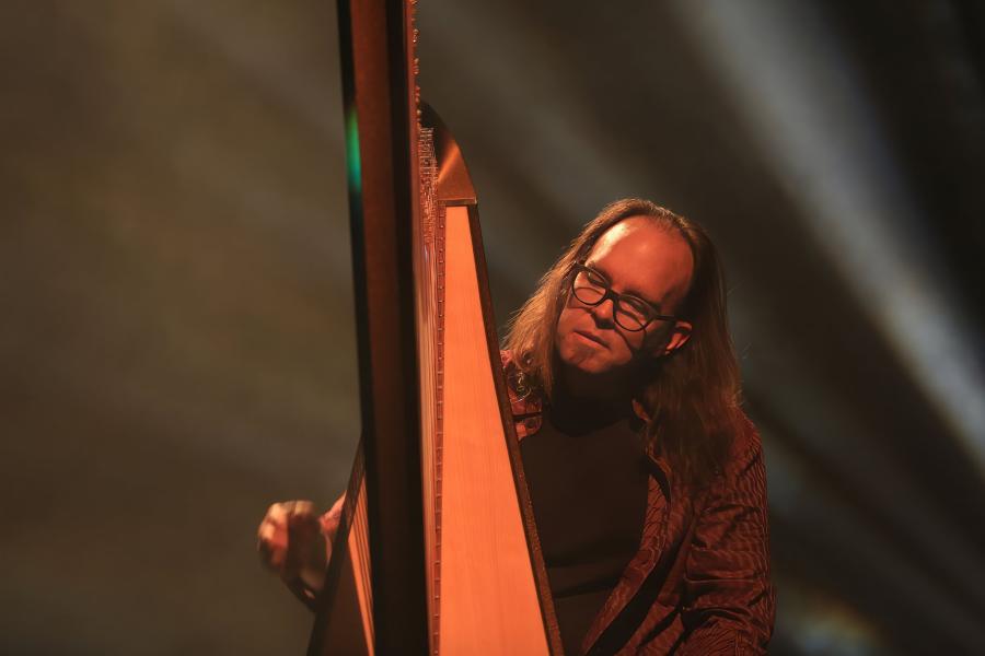 Harpist Park Stickney playing his harp with colorful stage lighting.