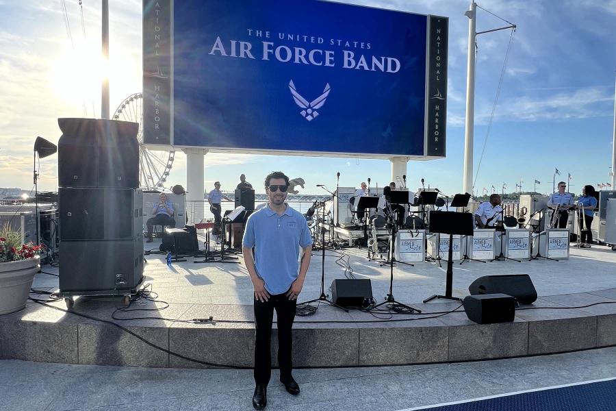  David Mesquitic on a ship with a stage and a Air Force Band sign in the background