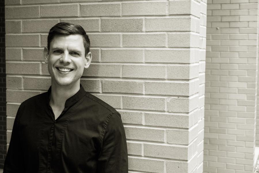 A black and white photo of Dr. Marc Sosnowchik standing in front of a brick wall, smiling.