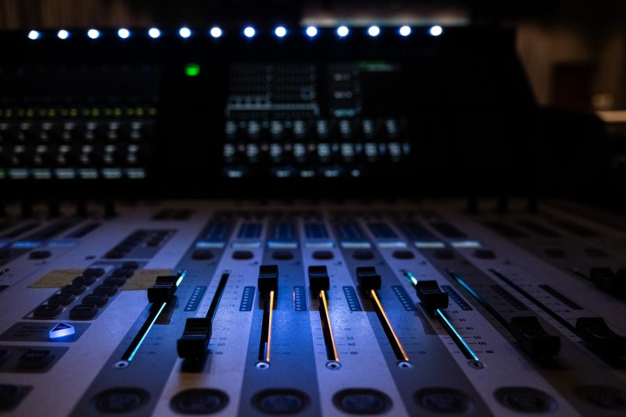 a close-up of a music mixing board, in a dark room with glowing lights