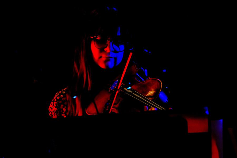 A violinist in the UT New Music Ensemble playing on a dark stage.