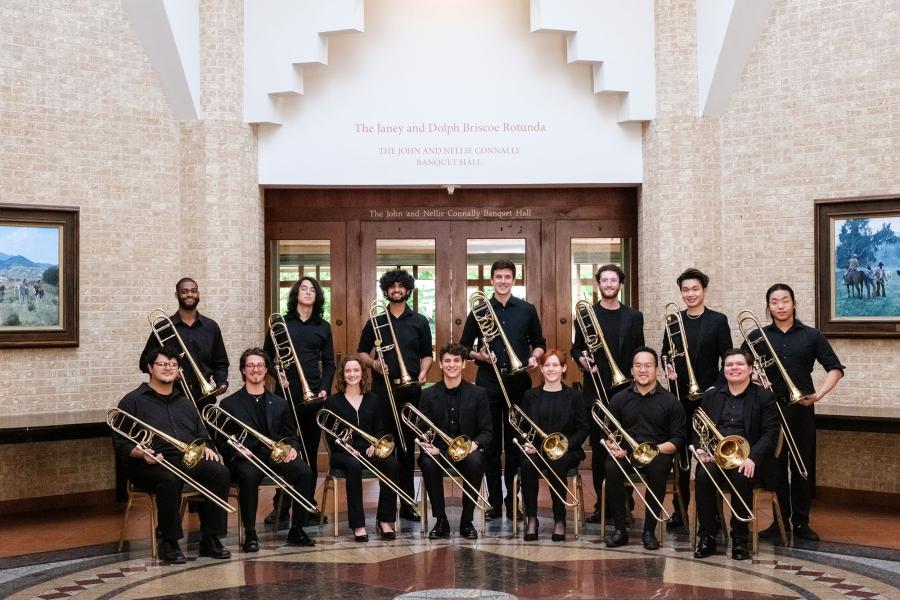 A group of students dressed in black holding trombones and posing in two rows in front of the doors to the John and Nellie Connelly Banquet Hall. 