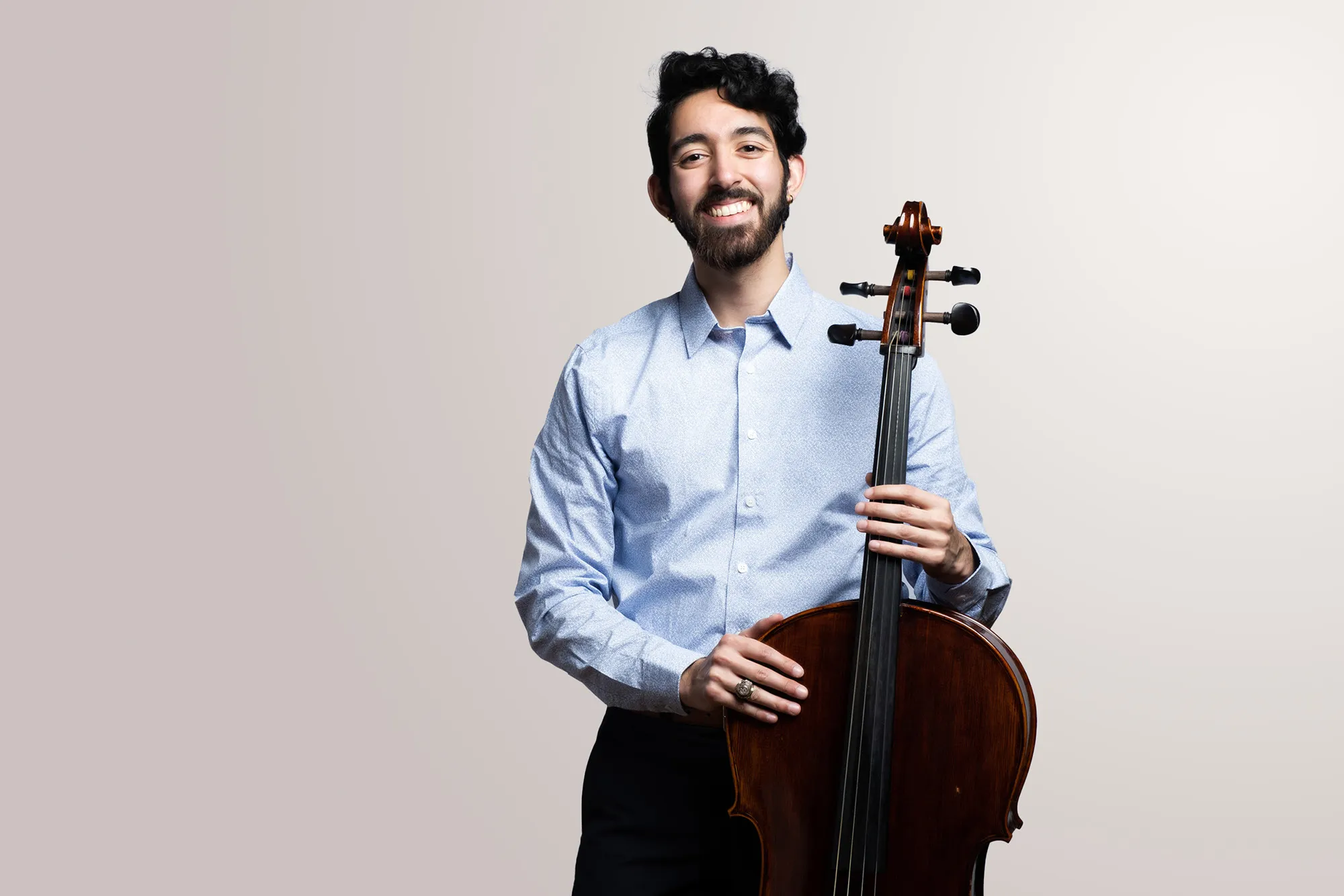 A Male cellist holds his instrument and smiles