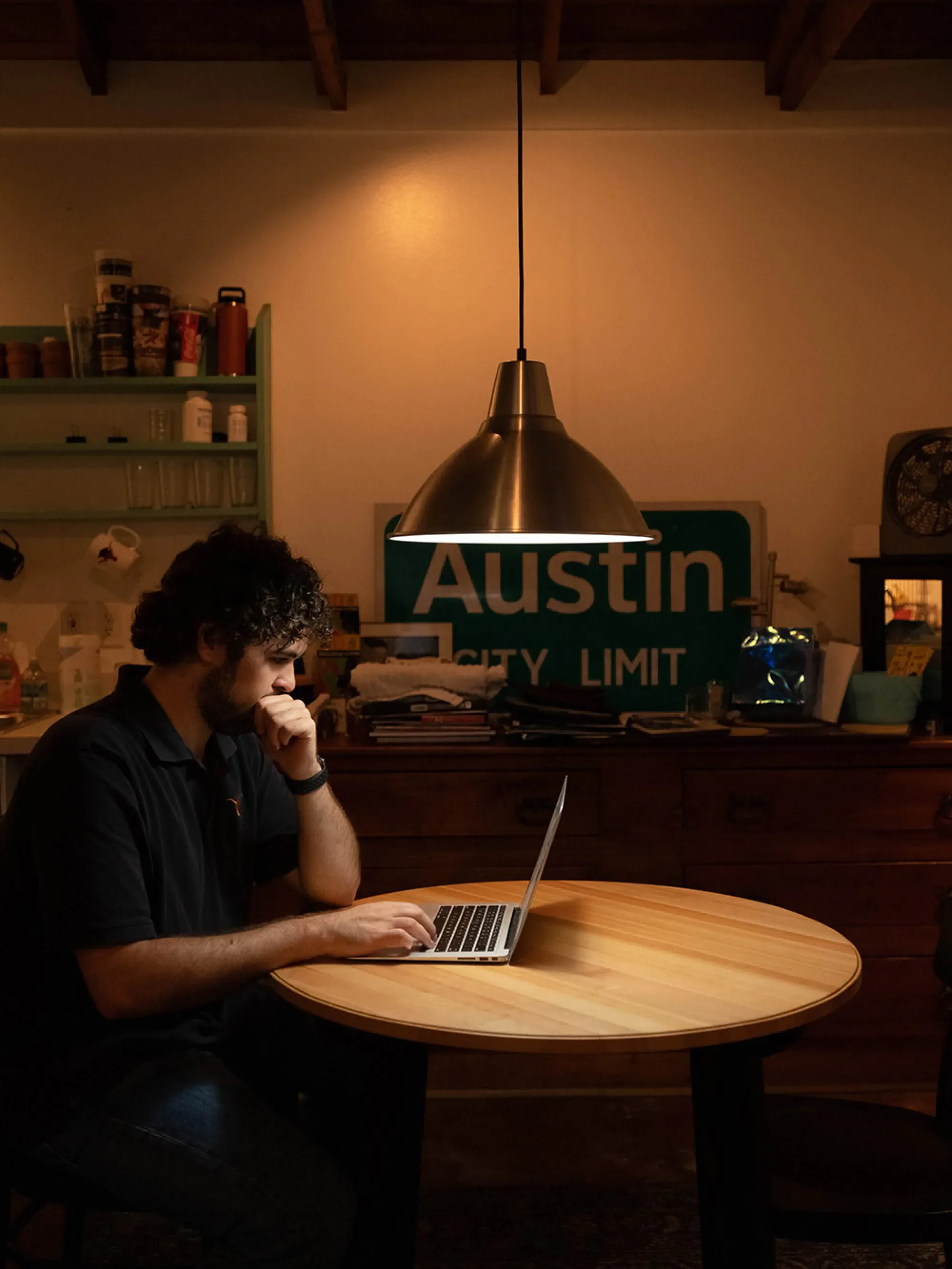 Nick sits at a daily lit table in his apartment kitchen, working on his laptop.