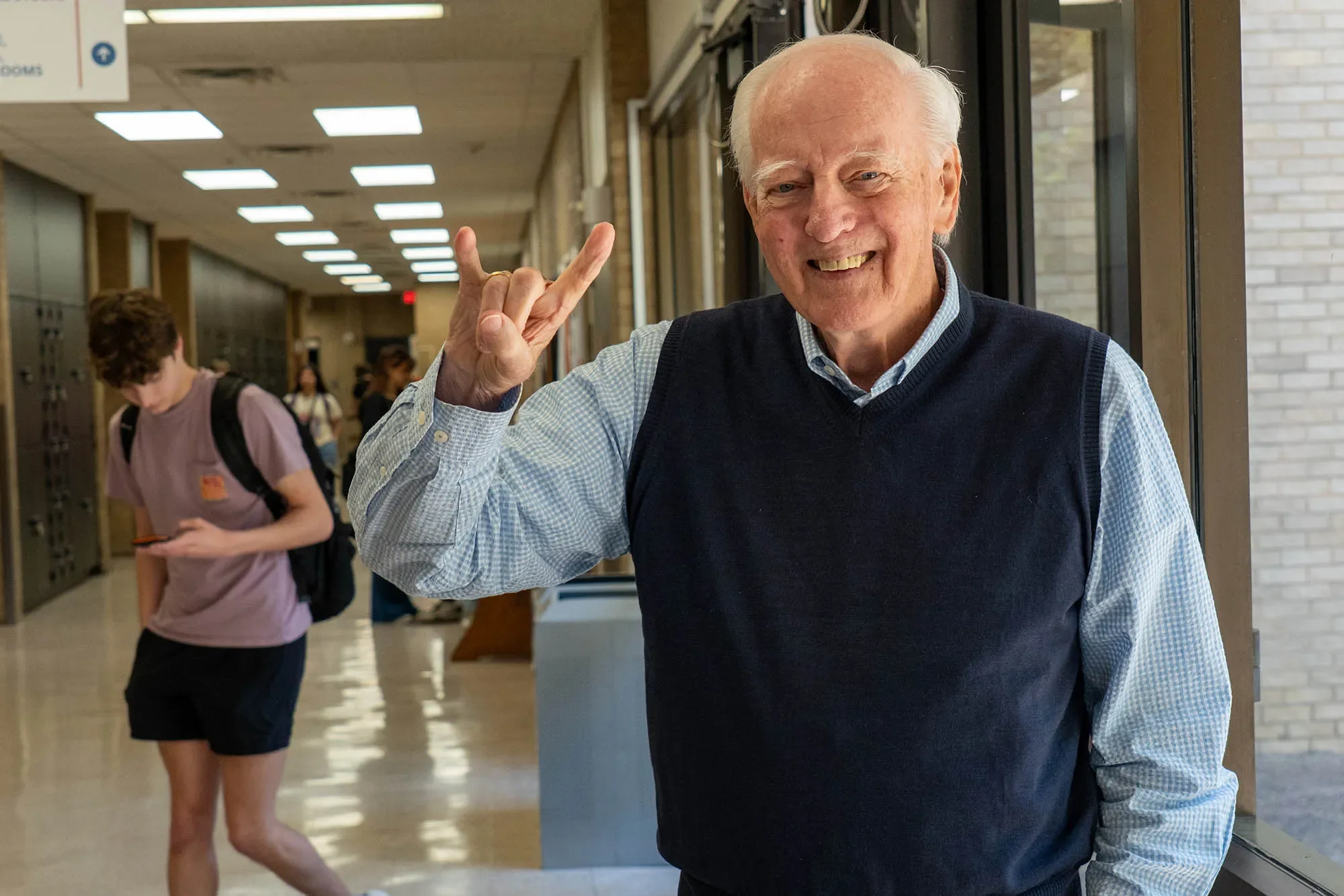 Thomas Lee showing the Hook em sign in a hallway