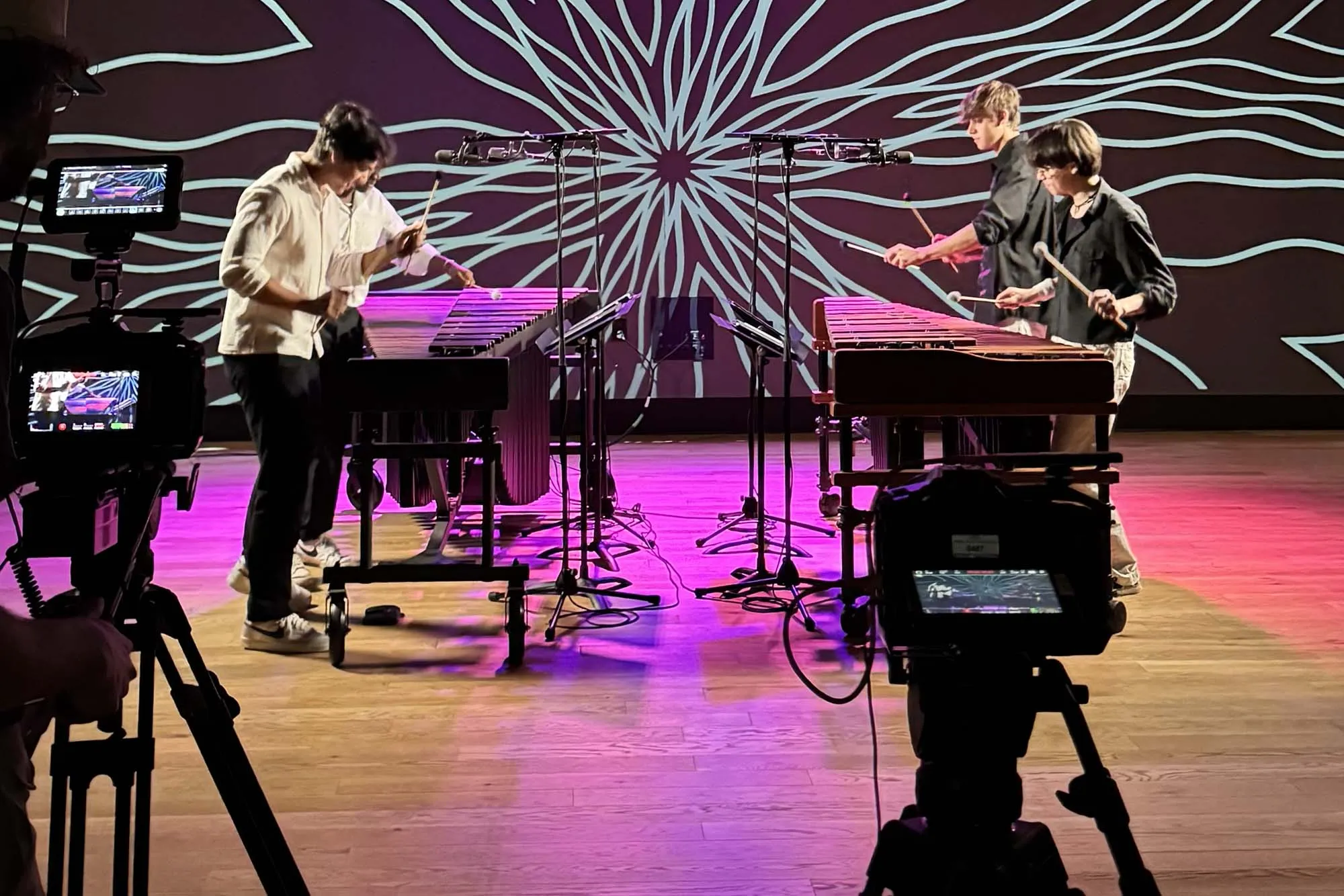 4 people playing percussion with a digital projection behind them