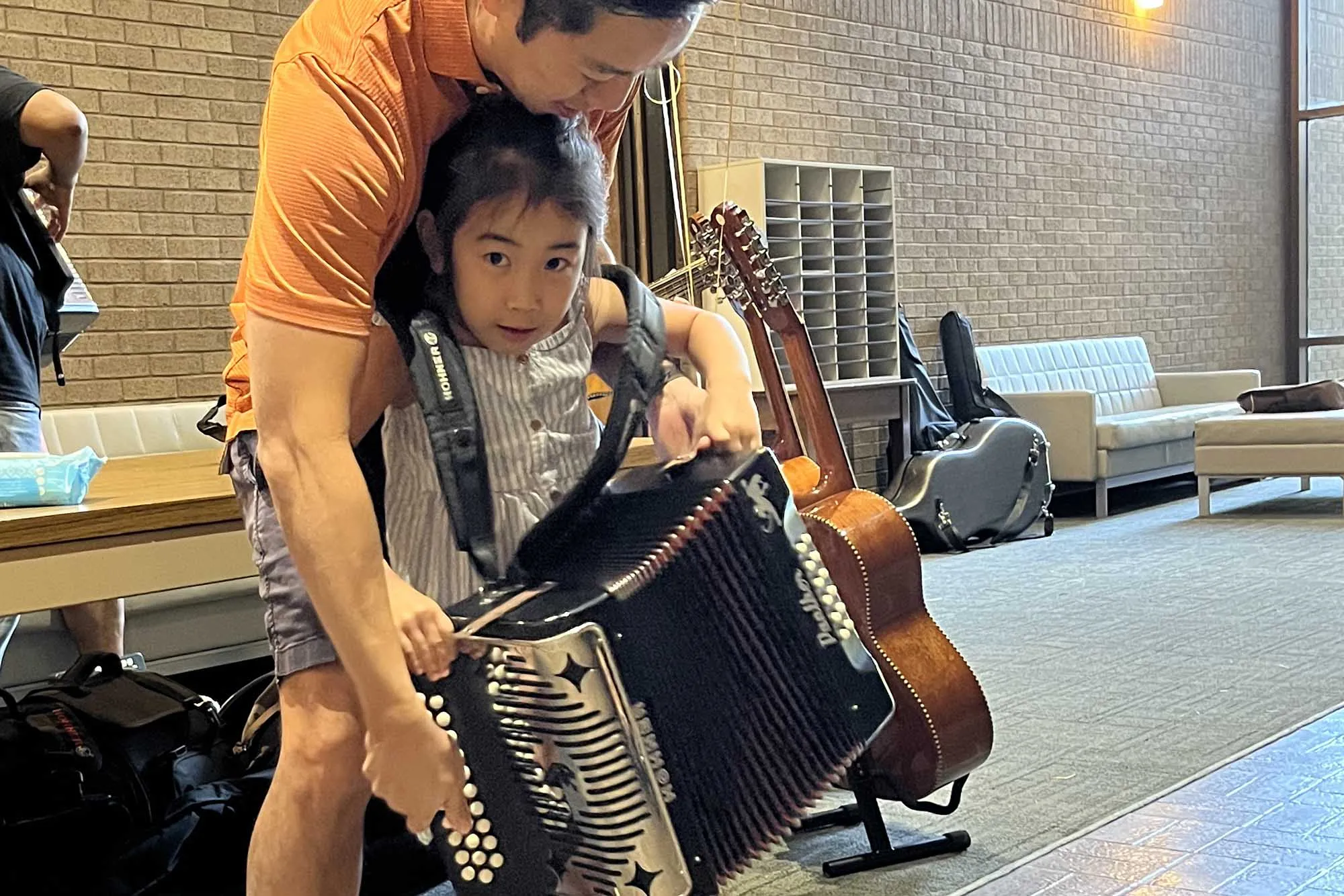 A child plays an accordion with the help of an adult