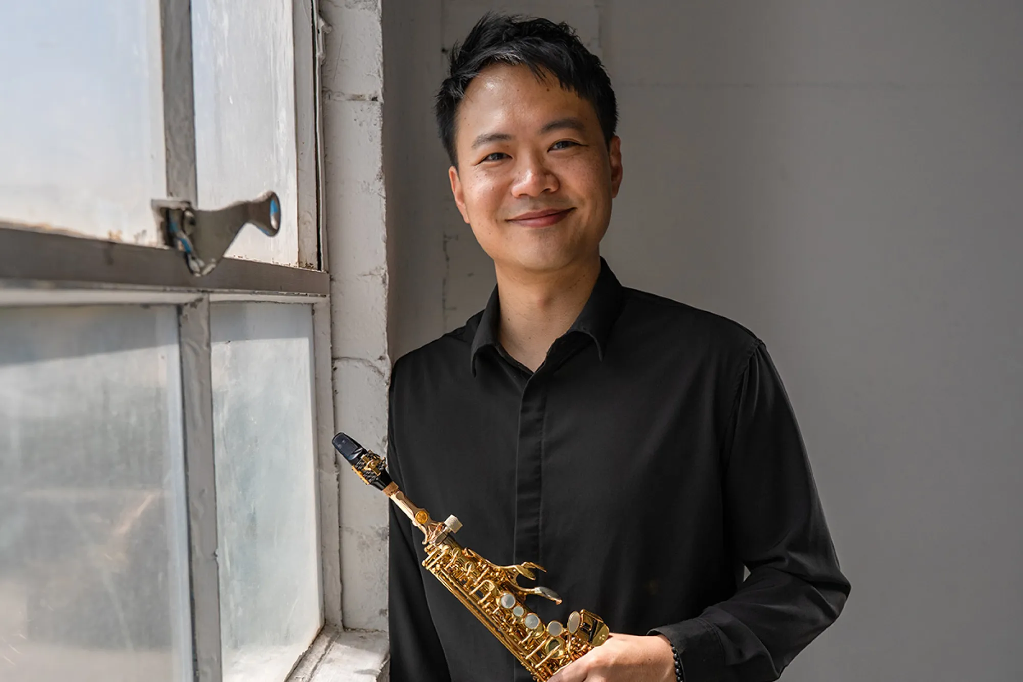 Calvin Wong posing with a sax in front of a window
