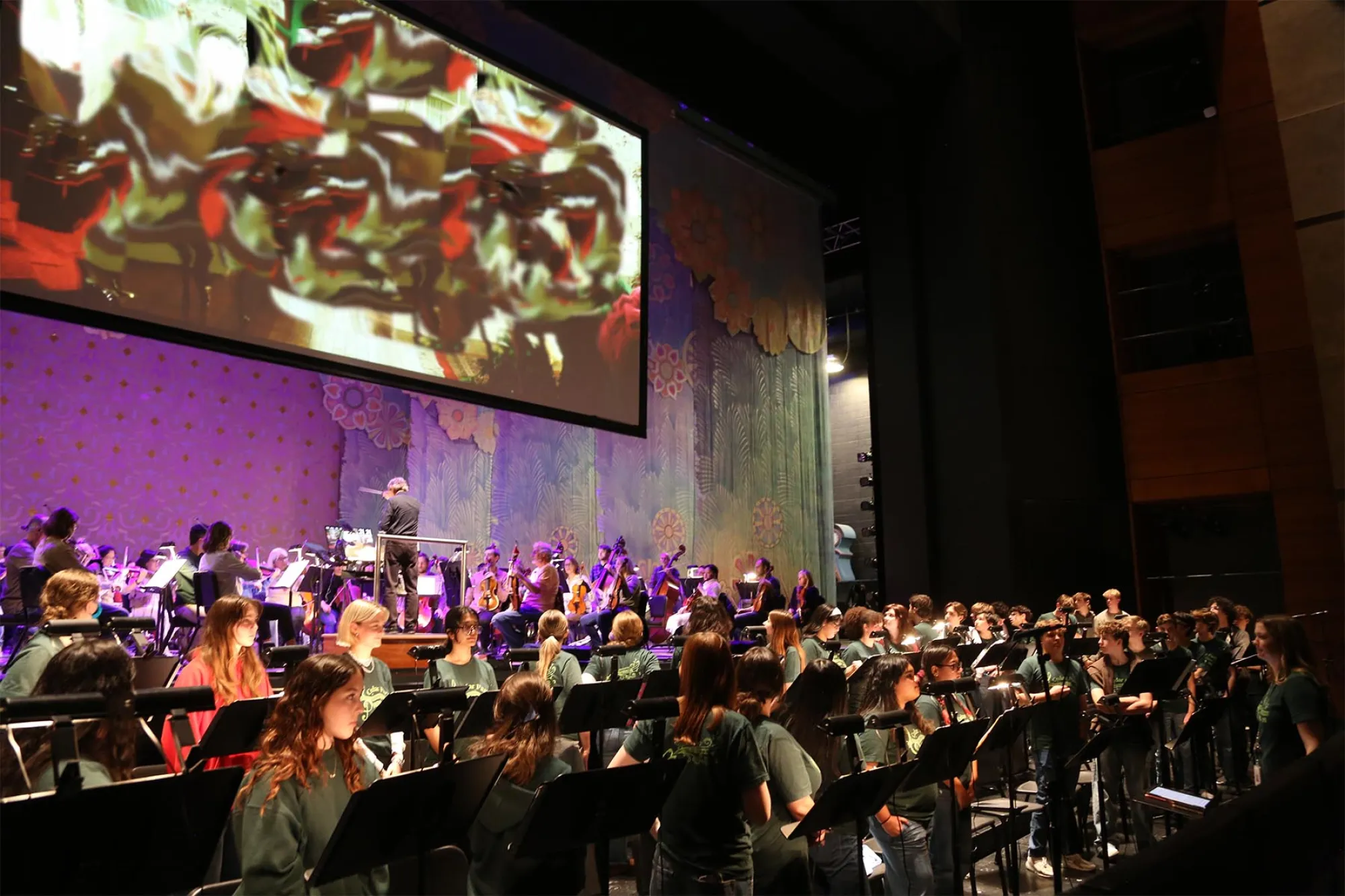 An orchestra plays under a giant movie screen