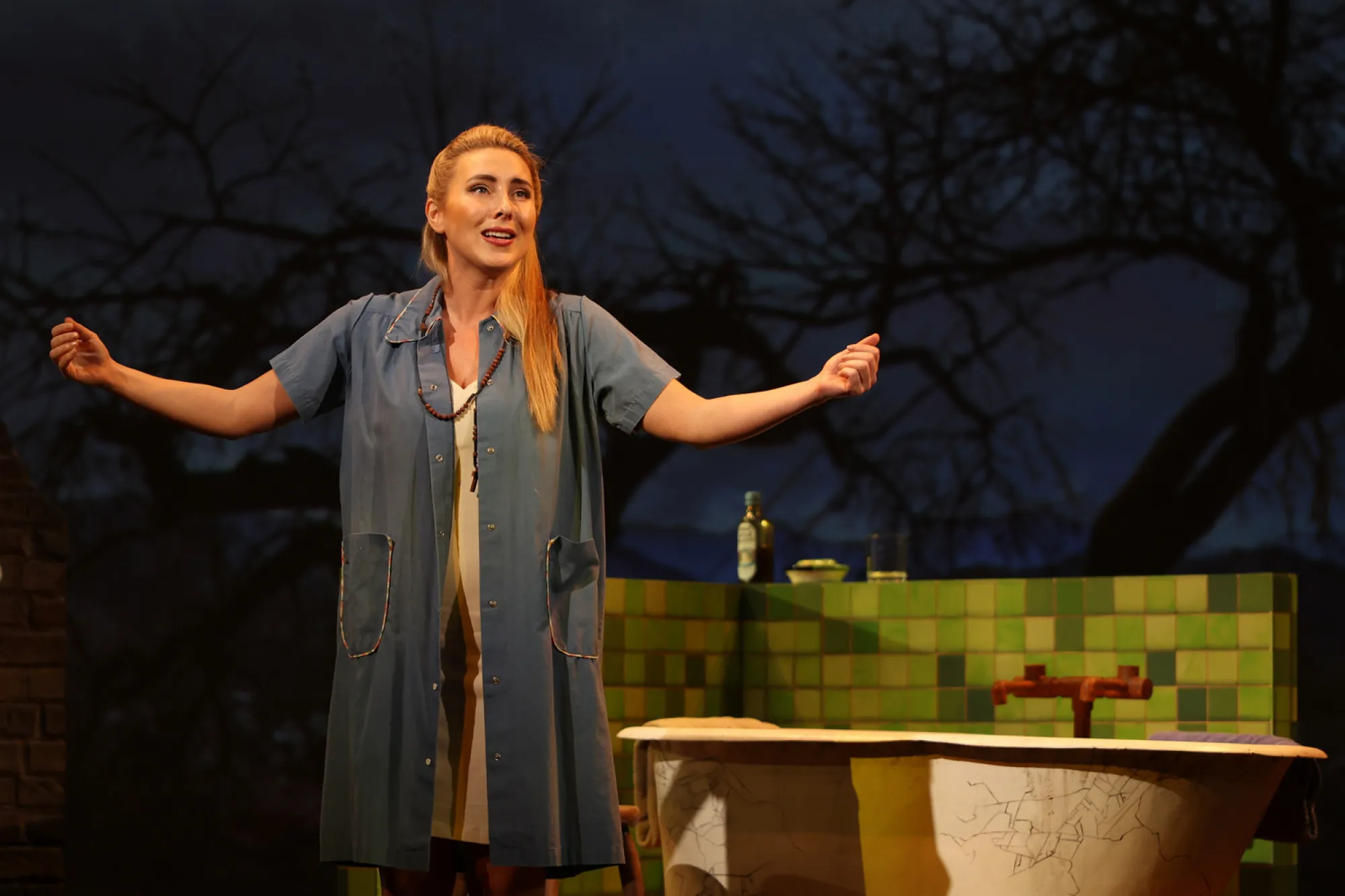 On stage a person singing outside in front of a bathtub 