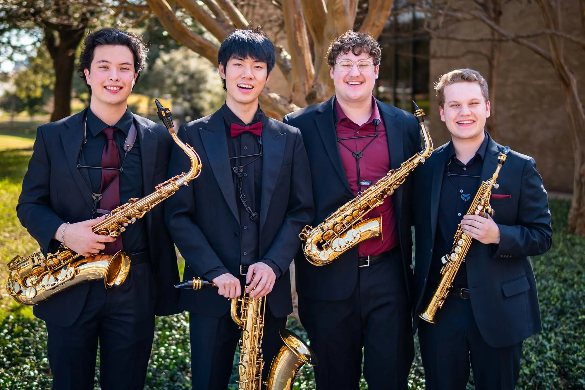 Wind quartet smile with a building in the background while holding saxaphones