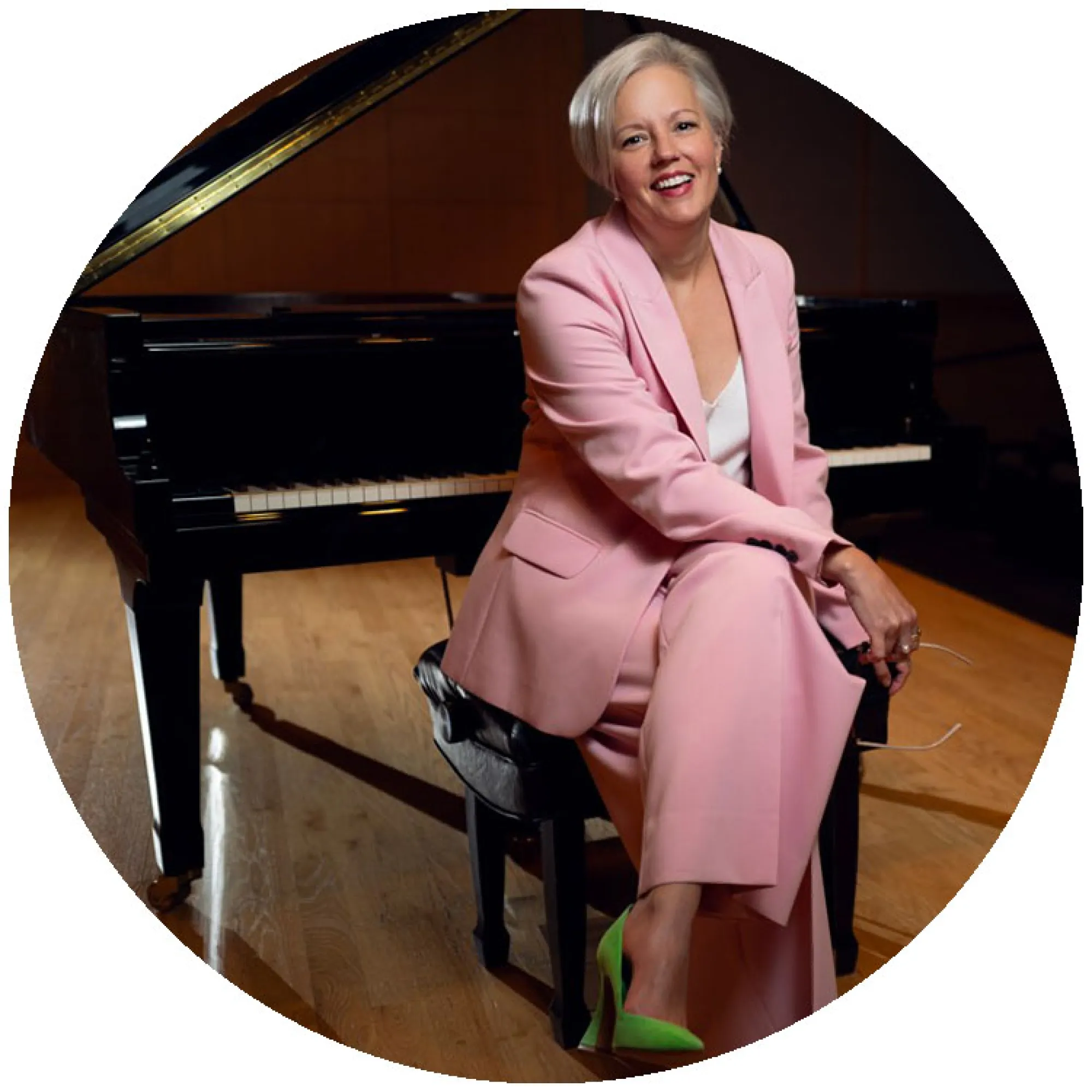 A publicity photo of Lee Anne Myslewski sitting on a piano bench with a concert grand piano behind her.