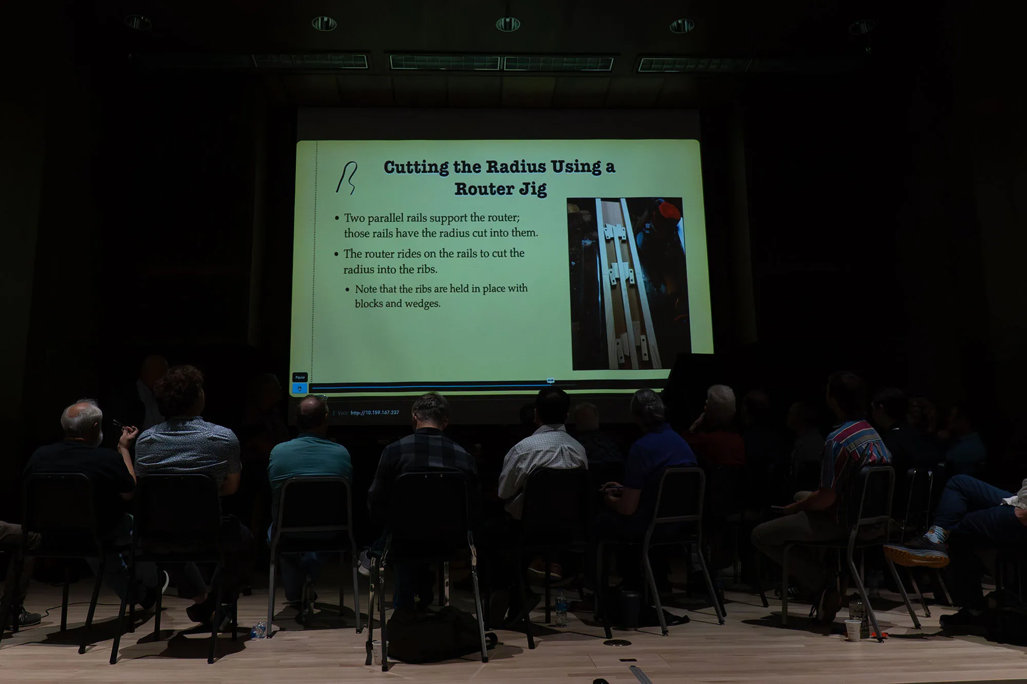 A group of people watch a screen about cutting wood
