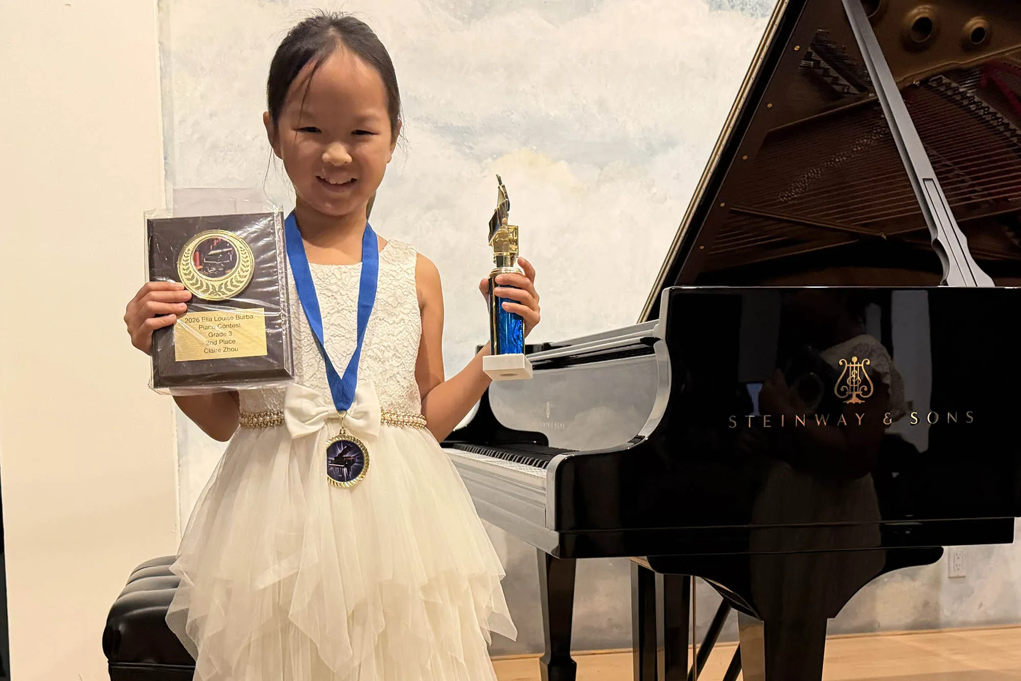 A young student holds an award with a piano in the background