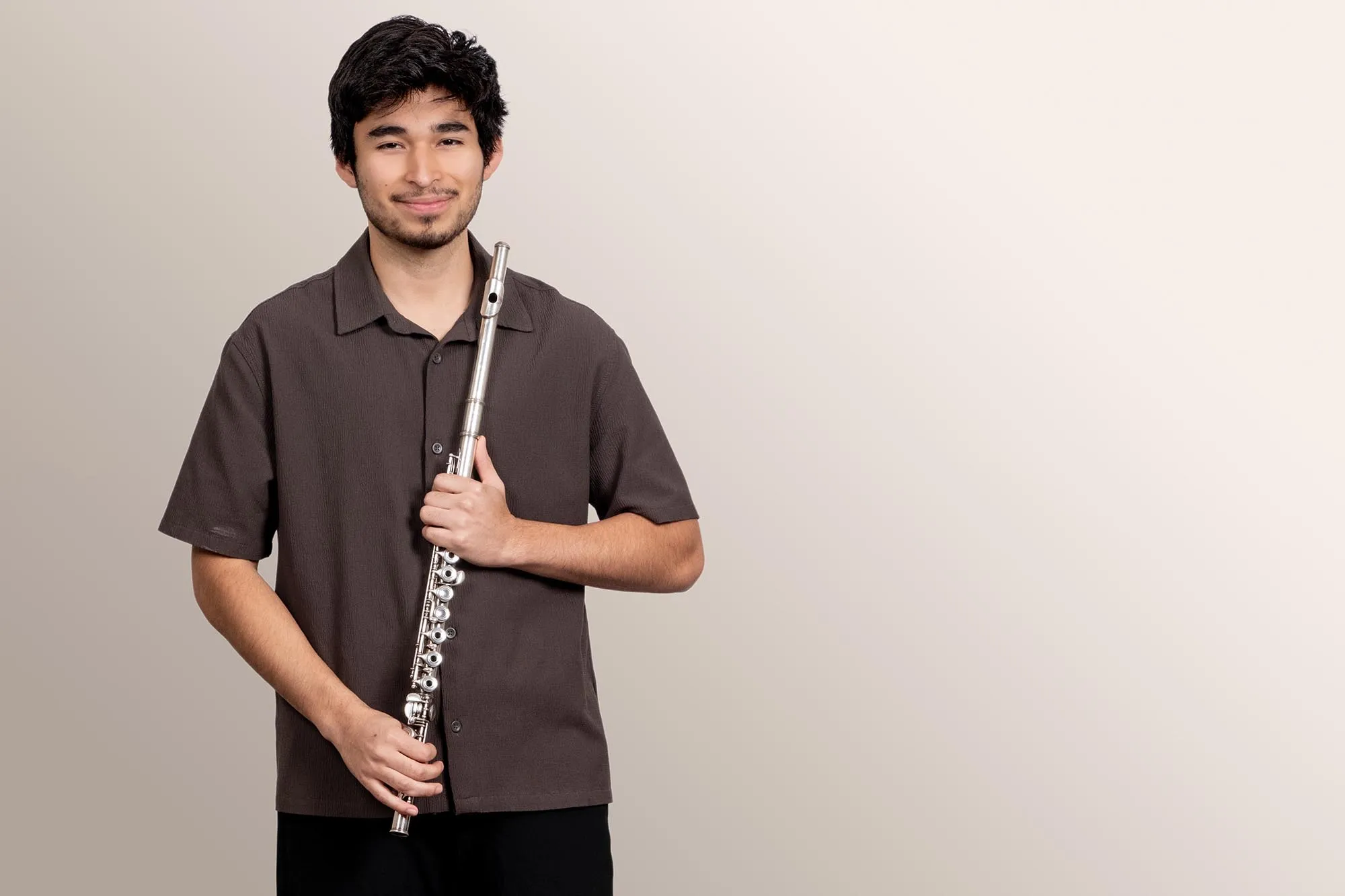A flute students smiles confidently at the viewer, holding his instrument