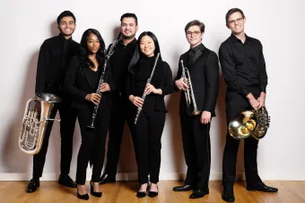Smiling Members of symphony band in concert attire posing with instruments