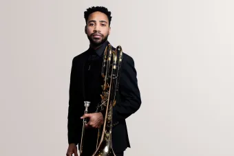 A trombonist holding his trombone looks confidently into camera