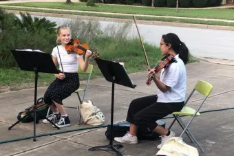 Lucy Hamre (left) and Ileana Nicholson (right) share a knowing look as they preform their violin arrangements for a socially-distanced audience.