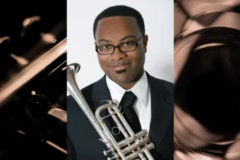 A black man wearing glasses holds a trumpet.