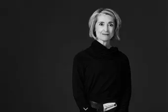 A black and white photo of a blonde woman wearing black with her arms crossed.