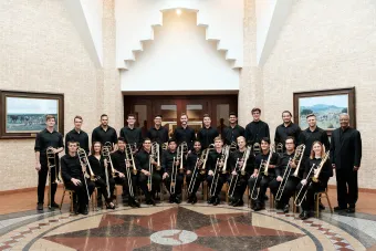 An image of the Trombone Choir holding their instruments in an elaborate hall