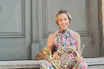A woman wearing a floral dress sits on steps with a horn in her lap.