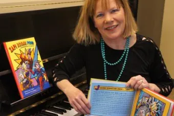 Lucy Amen Warner holds a copy of her children's book while sitting at a piano