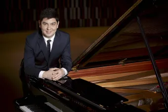 Pianist Behzod Abduraimov in a suit leaning on a piano