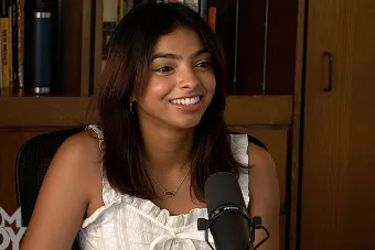 Ahana Bhat talking into a mic with a bookcase in the background