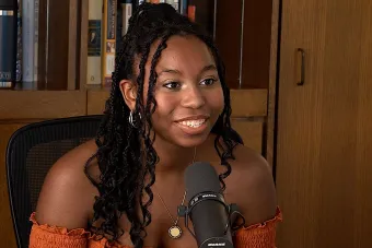 Pejah Carr talking into a mic with a bookshelf in the background