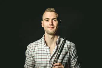 A headshot of clarinetist Tyler Webster wearing a checkered shirt holding his instrument.