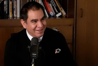 Diego Rivera talking into a mic with a bookshelf in the background