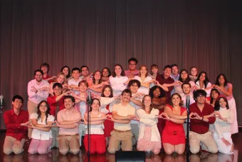 Members of the Longhorn Singers makes heart shapes with their hands and smile for the camera on stage.