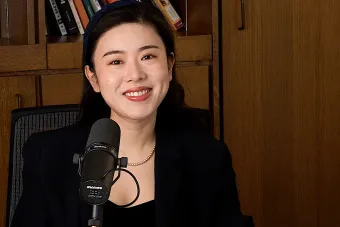 Jinni Shen talking into a mic with a bookshelf in the background