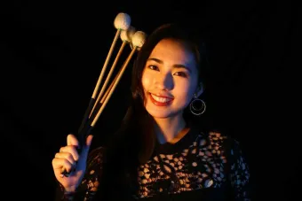 Person smiles while holding up drum mallets