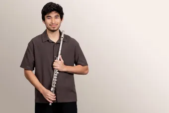 A flute students smiles confidently at the viewer, holding his instrument