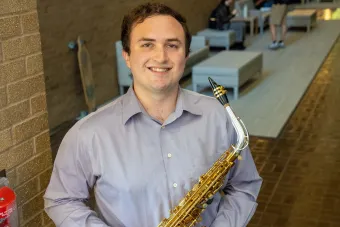 Andrew Stein holing a saxaphone with a hallway in the background