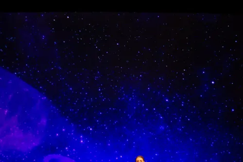 A singer and pianist perform on stage, behind a projection of a clear, starry night. High above them, the supertitles projection reads "Sleep, sleep, in they Sleep, little sorrows sit and weep."
