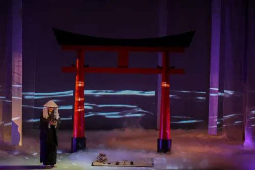 a shadowy figure stands on stage, at his feet is a traditional Chinese tea setting
